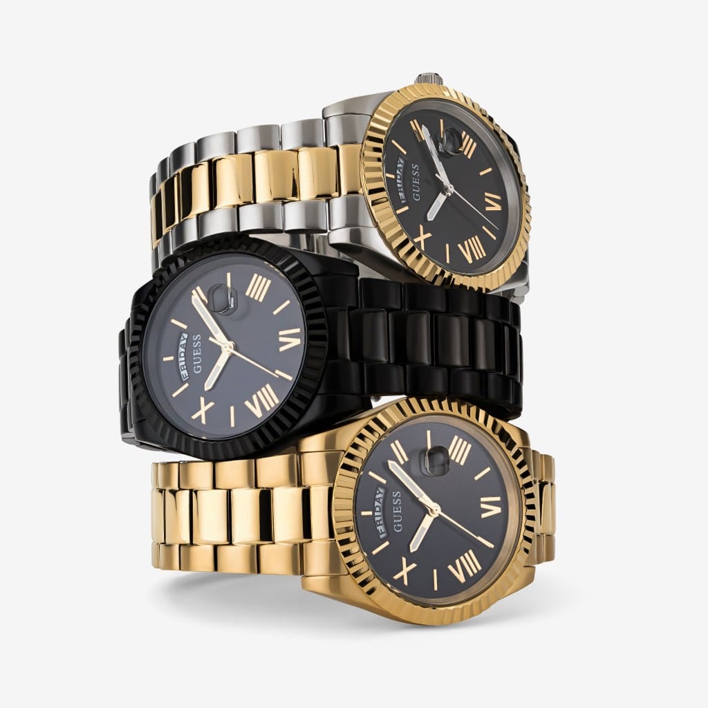 Stack of luxury wristwatches in gold, silver, and black metal bands on white background