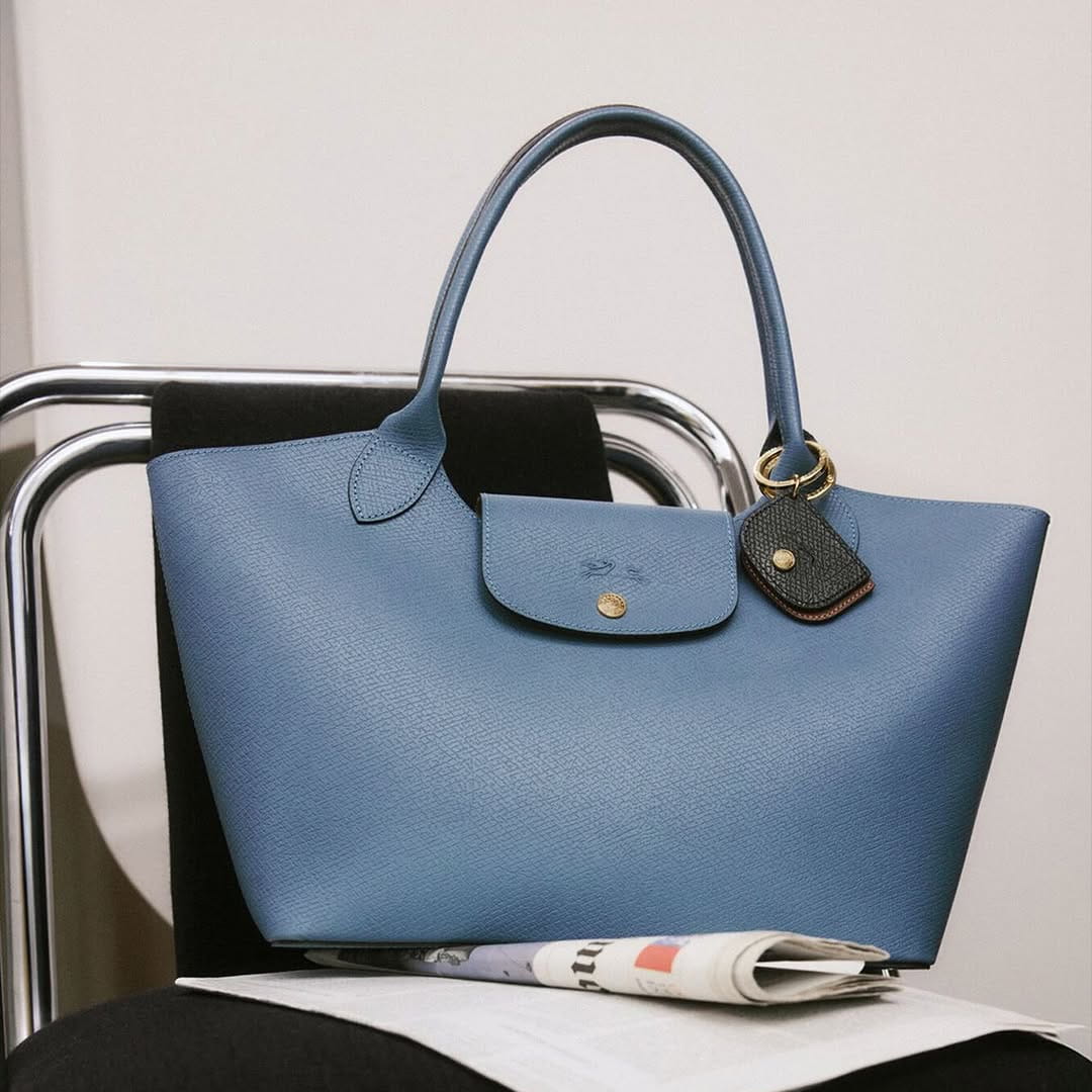 Blue structured leather tote bag styled on a modern chair with a magazine